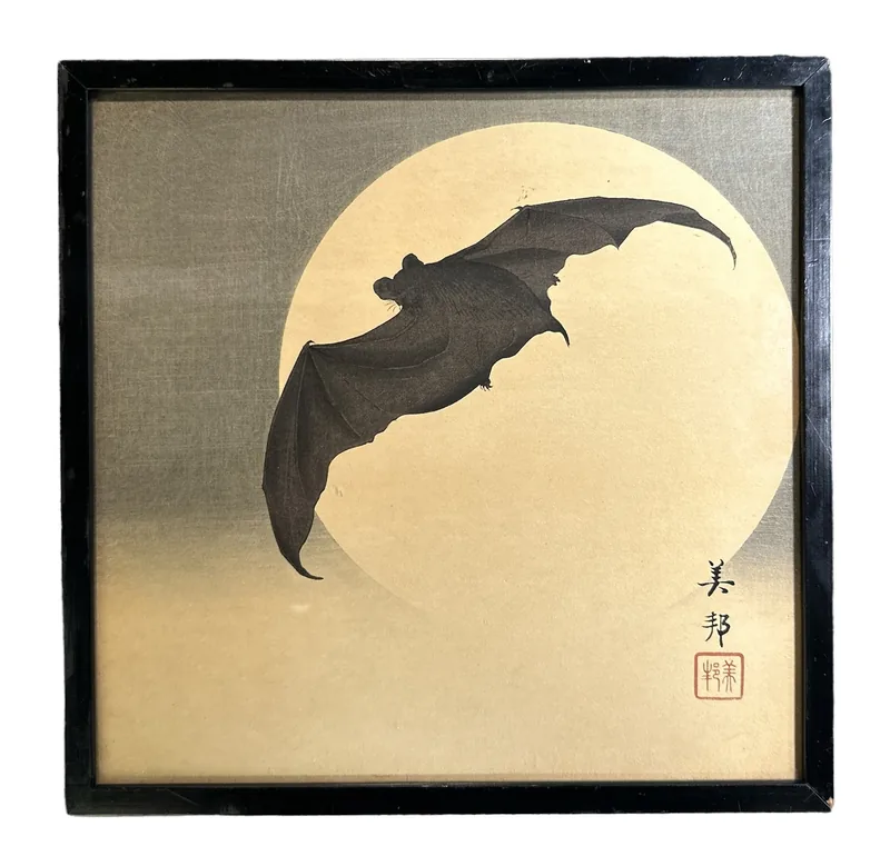 Un murciélago con las alas extendidas cruza una gran luna pálida sobre un fondo dorado, en un marco negro liso, con la firma y el sello del artista abajo a la derecha.